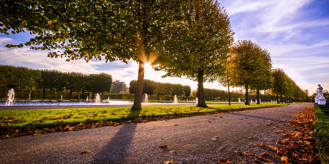 Allee in einem Park, im Hintergrund Brunnen.